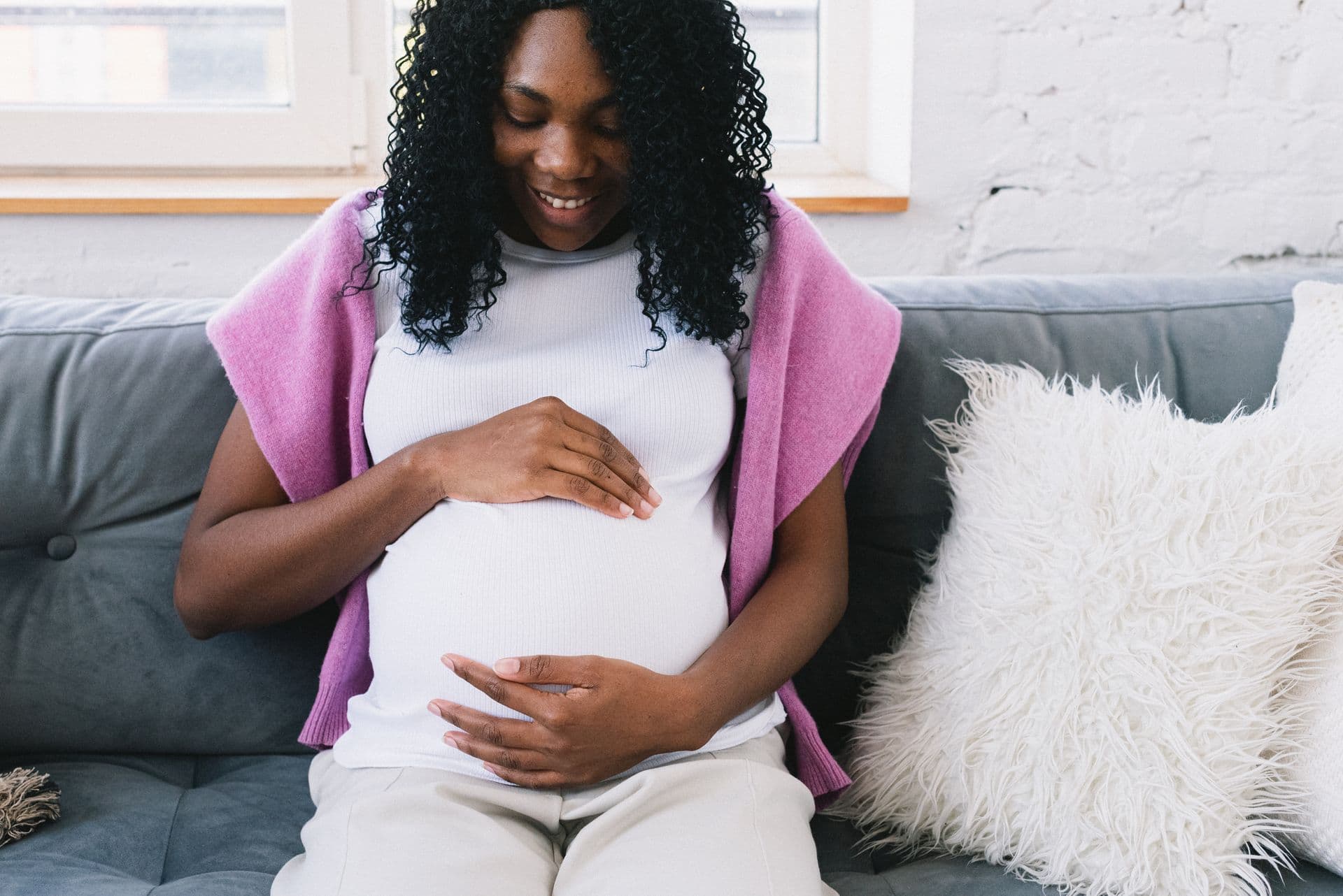 A woman on a sofa smiles at her pregnant belly